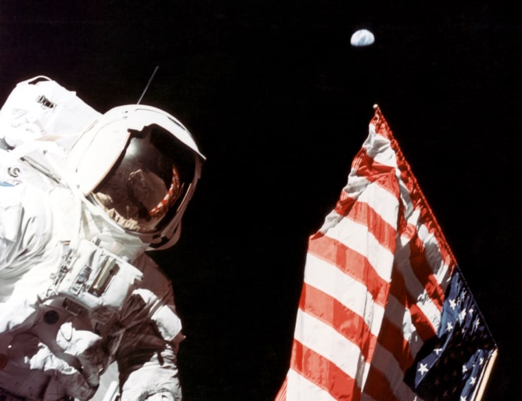 Apollo 17 astronaut Harrison Schmitt stands next to the U.S. flag on the lunar surface during a moonwalk at the Taurus-Littrow landing site in December 1972. Earth is visible in the far distance.
