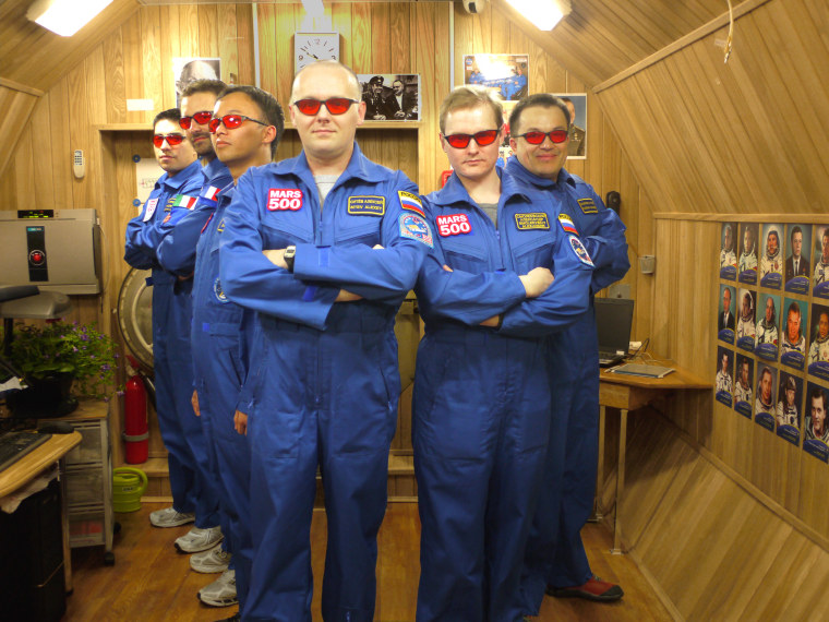 Crew members participating in the Mars500 simulated mission to the Red Planet strike a pose in their mock spaceship while wearing red-tinted glasses.
