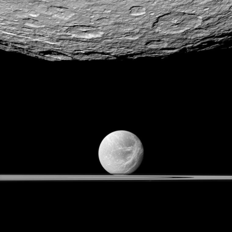 Cassini looks past the cratered south polar area of Saturn's moon Rhea to spy the moon Dione and the planet's rings in the distance.