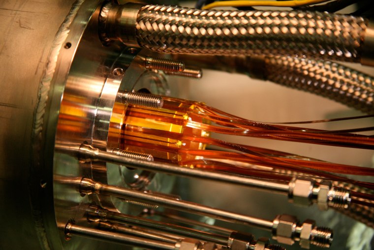 Gold electrodes are inserted into a vacuum chamber and cooling assembly. These electrodes are a key part of the trap in which positrons and antiprotons are