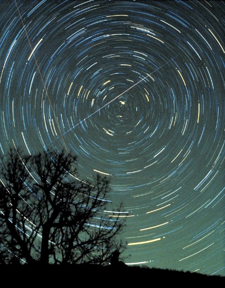 A Geminid meteor streaks across the night sky, with circular star trails whirling the background, in a time-exposure photo made by astronomer Jimmy Westlake in December 1985.