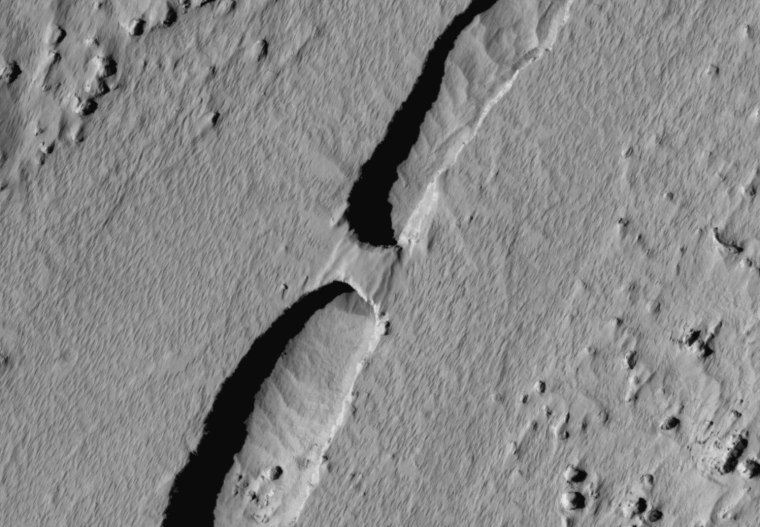 What appears to be a natural bridge spans a channel running through a geological feature on Mars known as Tartarus Colles.