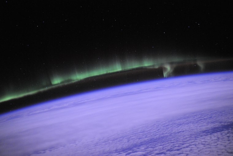 In a picture from the International Space Station, an auroral display flashes green above the violet haze on Earth.