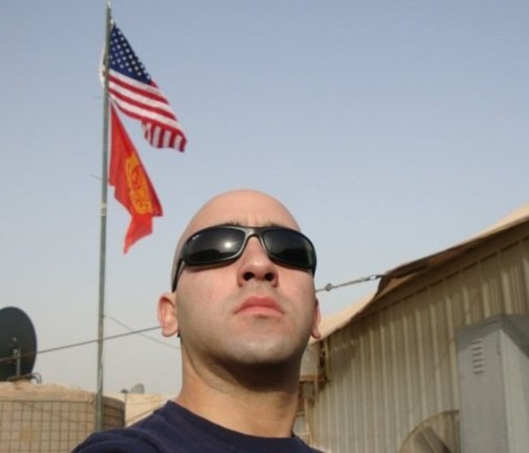 Jadiam Lopez in a government complex in Ramadi, Iraq, posing under a U.S. flag and a flag devoted to firefighters.