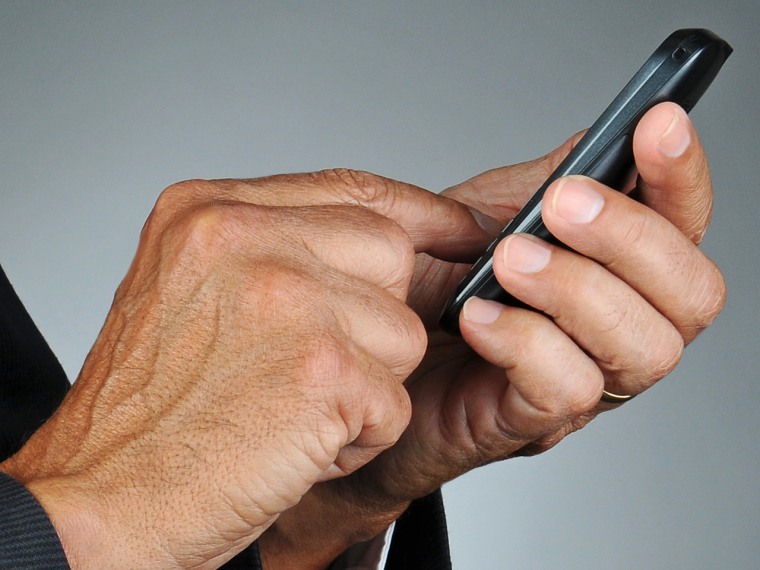 Closeup of a businessman dialing his cell phone. Horizontal format over a light to dark gray background. Man is unrecognizable.