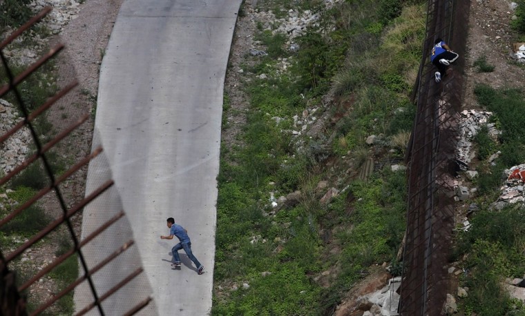 Two men illegally cross the border fence separating Nogales, Ariz., and Nogales, Sonora, Mexico on July 28, 2010.