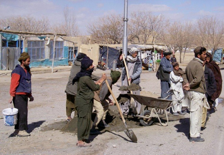 Afghan villagers help install solar-powered streetlights provided by the U.S. government.