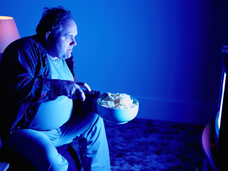 A man eats potato chips while watching TV.