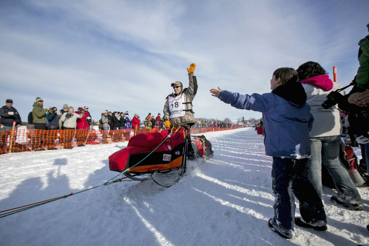 Four-time Iditarod champion Jeff King greets fans as his team charges down the trail at the start on March 3.