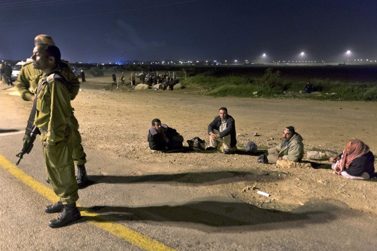Israeli soldiers stand on the roadside as Palestinians who have work permits wait for buses to take them to their jobs inside Israel before dawn on Monday.