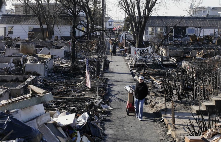 In this file photo, Louise McCarthy carts belongings from her flood-damaged home as she passes the charred ruins of other homes in the Breezy Point section of the Queens borough of New York, Nov. 14. A fire destroyed more than 100 homes in the oceanfront community during Superstorm Sandy.