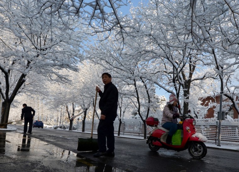 Workers clear snow on the side of a road as a commuter drives past in Beijing.
