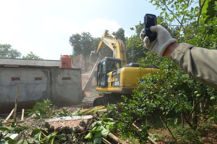 An Indonesian civilian policeman takes photographs while an excavator demolishes an under-construction building of the Taman Sari Batak Christian Protestant Church in Bekasi on March 21, 2013.