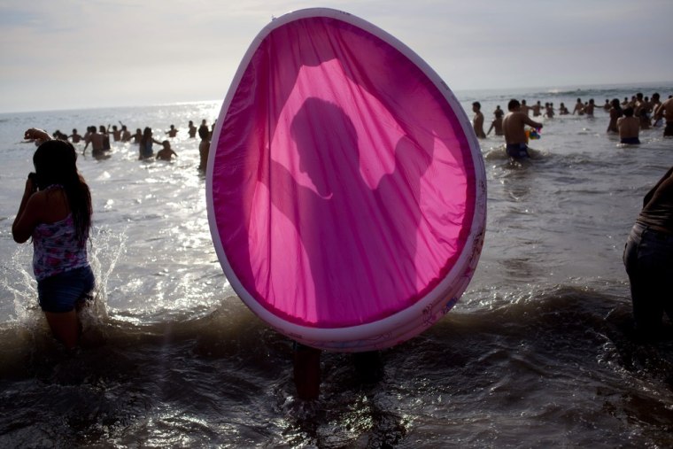 A man is silhouetted in a wading pool as he cleans it out in the ocean waters off Agua Dulce beach in Lima, Peru.