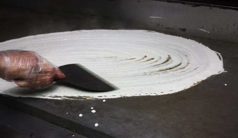 Dosa batter cooks on the griddle.