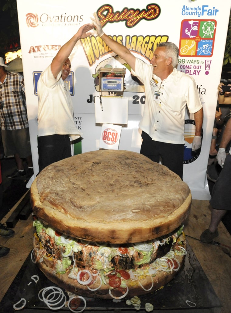 In this photo taken Saturday, July 2, 2011, Brett Enright, of Phoenix, with Juicy's Outlaw Grill, left, and Nick Nicora, of Castro Valley, with Ovations Food Services, celebrate after making a Guinness World Record for the World's Largest Commercially Available Hamburger.
