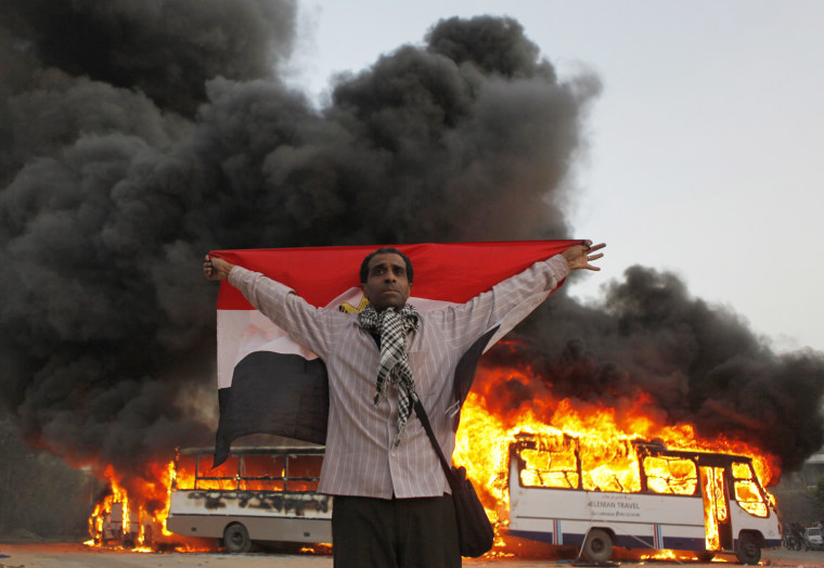 An anti-Mursi protester stands with the national flag after protesters burned Muslim Brotherhood buses during clashes near the Muslim Brotherhood's national headquarters in Cairo's Moqattam district on March 22, 2013.