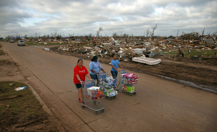 Image: Volunteers Jaqi Castro, Angelica Morris-Smith and Cetoria Petties walk through a tornado ravaged neighborhood handing out s...