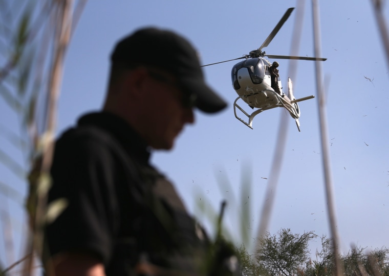 A U.S. Office of Air and Marine agent stands over a drug smuggler on the bank of the Rio Grande River at the U.S.-Mexico Border on April 11, 2013 in Mission, Texas. Agents with helicopter support from the U.S. Office of Air and Marine broke up a marijuana smuggling operation from Mexico into Texas.