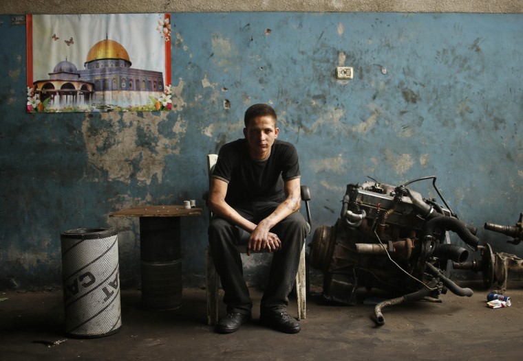 Palestinian Ali al-Batniji, 18, poses in an auto repair garage in Gaza City on May 30, 2013. A picture of the Dome of the Rock shrine and Al-Aqsa mosque in Jerusalem's Old City hangs in the background.