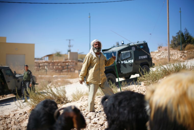 Suleiman Khatarin, a shepherd from the Palestinian village of Umm al Kheir, herds his goats close to the Israeli settlement of Carmel as Israeli soldiers and police look on.