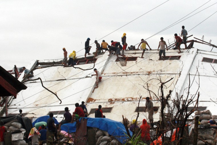 Typhoon survivors climb on a damaged warehouse belonging to the National Food Authority in Alangalang, Philippines, on Tuesday.