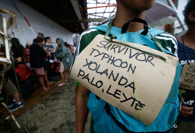 Typhoon survivors hang signs from their necks as they queue up in the hopes of boarding a C-130 military transport plane, Nov. 12, 2013, in Tacloban, central Philippines. Thousands of typhoon survivors swarmed the airport seeking a flight out, but only a few hundred made it.