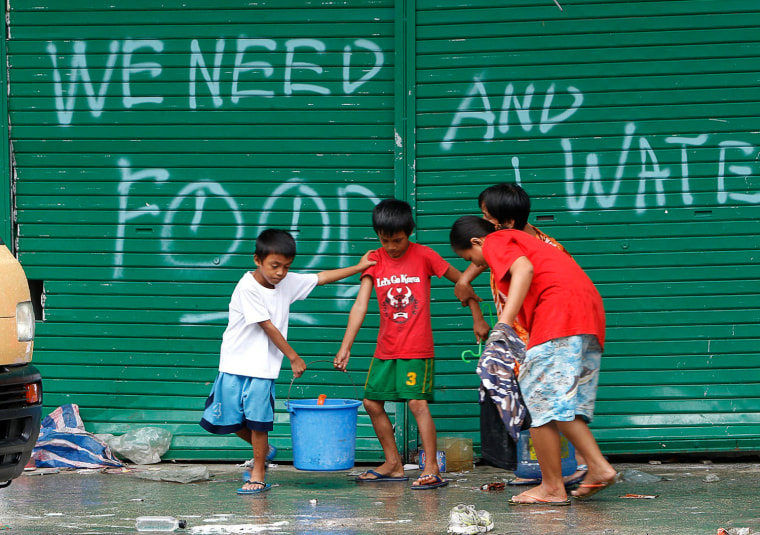 Children help to carry pails of drinking water as they walk past graffiti calling for help in Tacloban city, central Philippines Nov. 12, 2013.