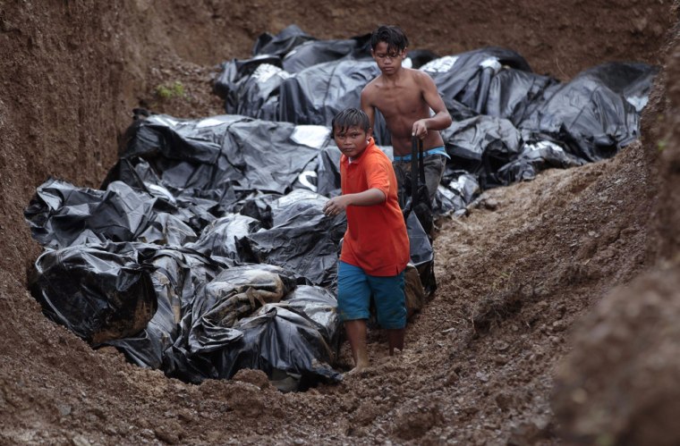 Two boys help to fill a large grave with body bags in the devastated city of Tacloban, Philippines on Thursday.