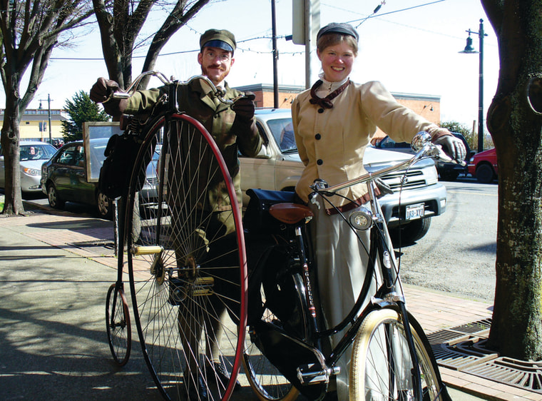 Chrisman and her husband in Victorian-era attire, riding bicycles of the period.