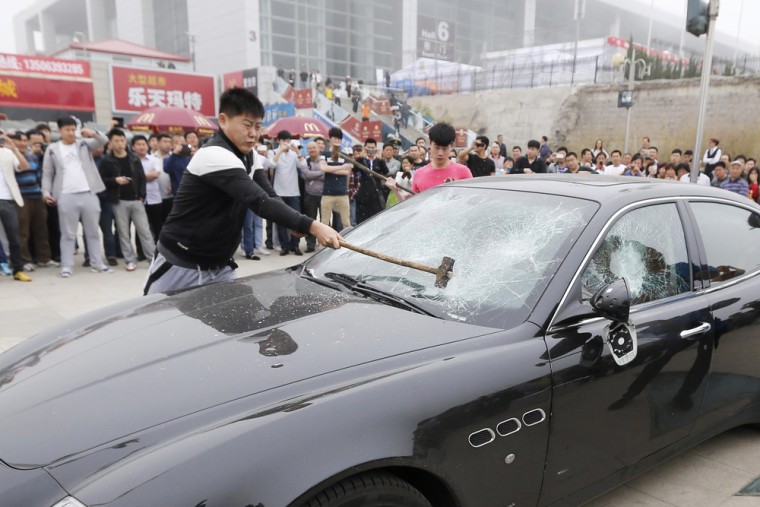 Talk about tuhao! This picture taken on May 14, 2013 shows men using sledgehammers on a Maserati car outside the Qingdao International Convention Cent...
