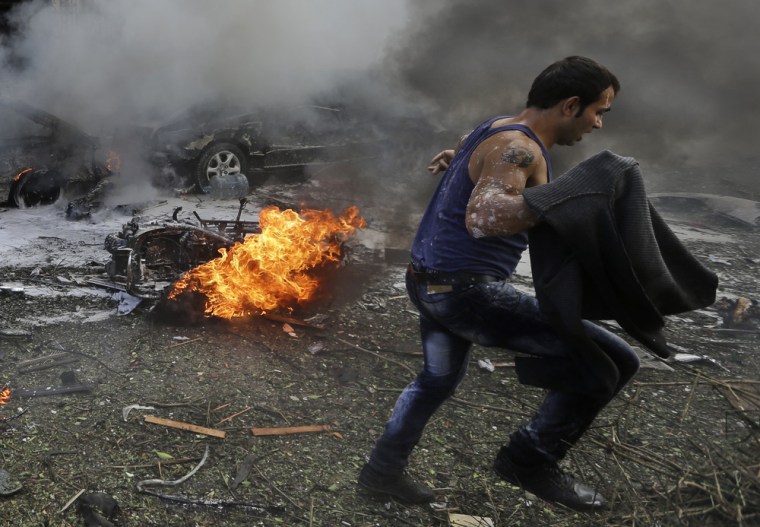A man runs in front of a burned car at the scene of explosions near the Iranian Embassy in Beirut, Tuesday.