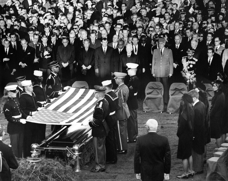 Service members fold the U.S. flag for President John F. Kennedy at his gravesite at Arlington National Cemetery, Va., on Nov. 25, 1963. In attendance, right side, front to back: Jacqueline Kennedy, Robert F. Kennedy, Eunice Shriver, Patricia Lawford, Jean Smith, Superintendant of the Arlington National Cemetery Jack Meltzer. Front row middle to right: President of West Germany Heinrich Luebbe, Gen. Charles de Gaulle of France, Emperor of Ethiopia Haile Selassie, President of the Phillipines Diosdado Macapagal, and other unidentified mourners.