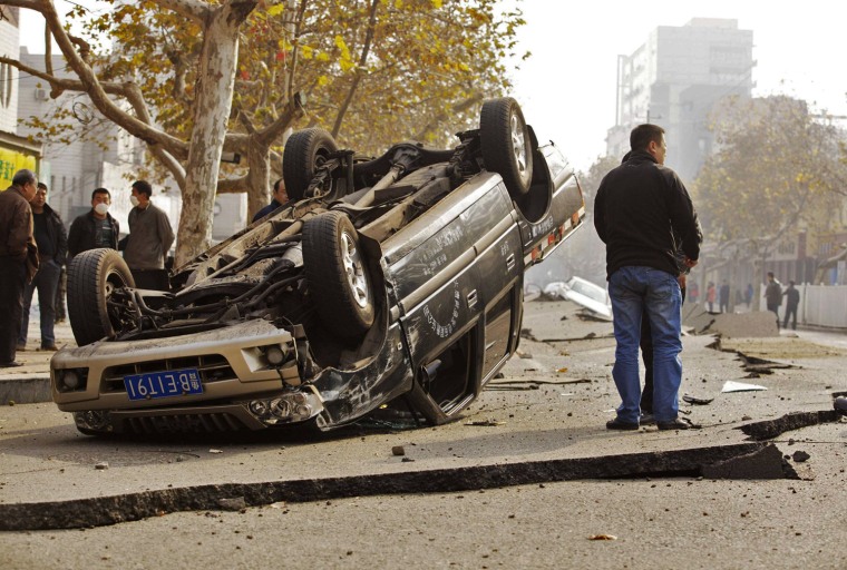 A man stands next to an overturned car on a street damaged by an explosion at a Sinopec Corp oil pipeline in Qingdao, China, on Friday.