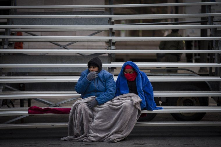 Crystal Nix, left, and Destiny Golden brave the cold while sitting on bleachers as they wait for the parade.