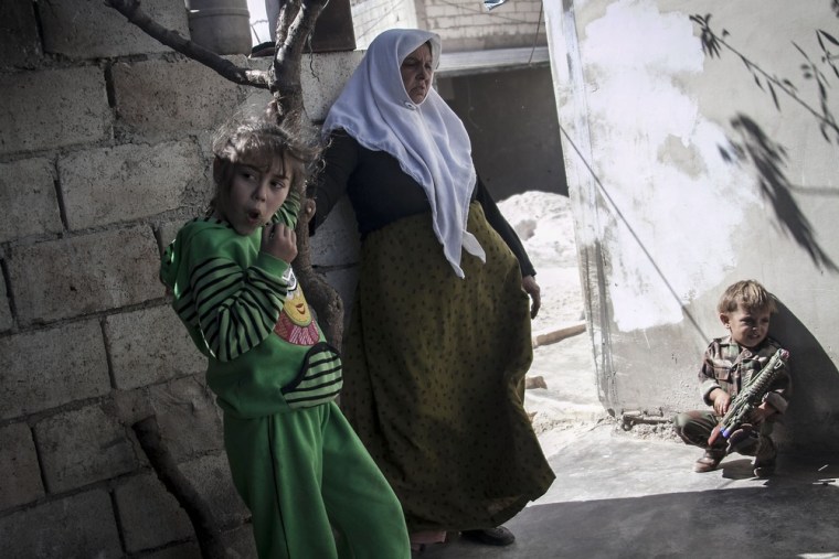 The wife of Mohammed Kale stands with her granddaughter and grandson in the yard of their house.