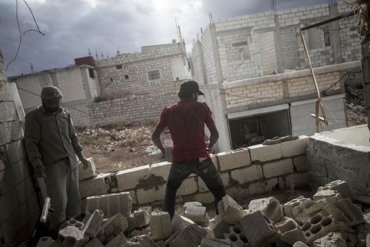 Sons of Mohammed Kale rebuild a wall damaged by a mortar shell at their family home.