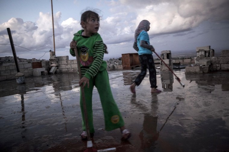 A girl reacts to the buzz of stray bullets overhead as she cleans the roof of her family house in Kfar Lata, a town that comes under heavy bombardment due to the fighting between opposition fighters and government forces in Syria's Idlib province.