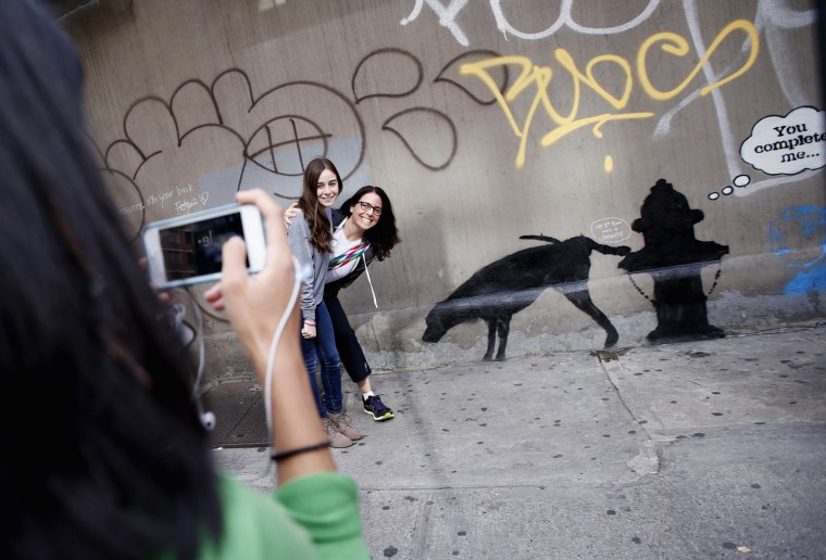 Two women have their picture taken next to new artwork by British graffiti artist Banksy on West 24th street in New York City.