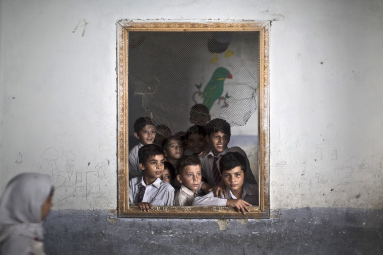 Pakistani schoolboys look out the window of their classroom at other classmates chanting  prayers to commemorate the anniversary of Malala's shooting at a school in Rawalpindi, Pakistan, on Wednesday.