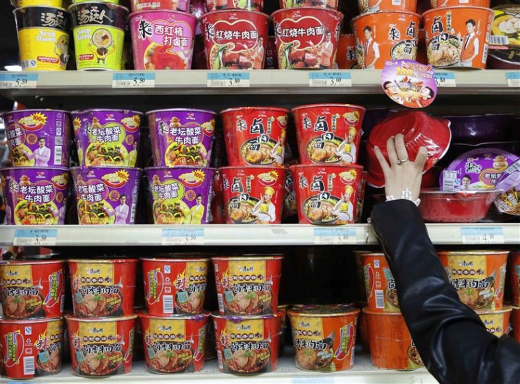A woman chooses a cup noodle from a shelf displaying cup noodles from Uni-President China (top and middle) and Tingyi (bottom) at a supermarket in Bei...