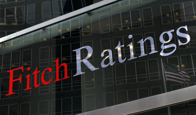 A flag is reflected on the window of the Fitch Ratings headquarters in New York in this Feb. 6, 2013, file photo. Fitch Ratings warned on Tuesday that it could cut the sovereign credit rating of the United States from AAA, citing the political brinkmanship over raising the federal debt ceiling.