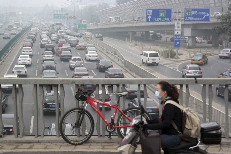 A woman wearing a protective mask rides on a scooter along a overpass with heavy car traffic below during a very polluted day in Beijing on Oct. 6, 2013.