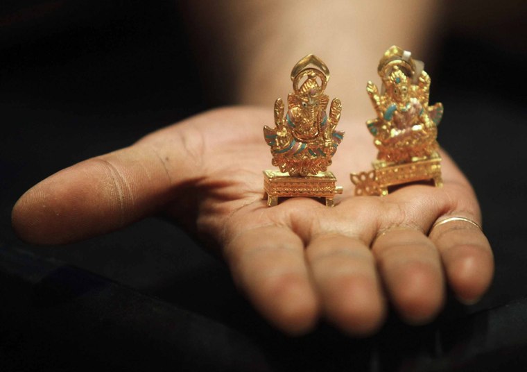 An example of India's vast appetite of gold, a worker at a jewelry showroom in Kolkata displays idols of Hindu elephant god Ganesh, left, and Hindu goddess Lakshmi.