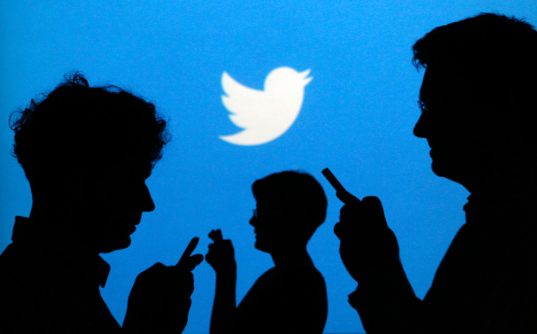 People holding mobile phones are silhouetted against a backdrop on which the Twitter logo is projected, in this file picture illustration taken in War...