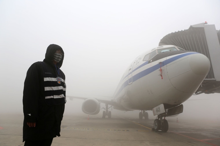 A man stands next to an airplane under heavy smog in Harbin.