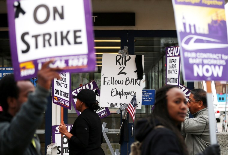 Striking Bay Area Rapid Transit (BART) workers picket in front of a sign on Oct. 21 honoring two BART workers who were struck and killed by a BART train over the weekend while servicing tracks near the Walnut Creek in Oakland, Calif.