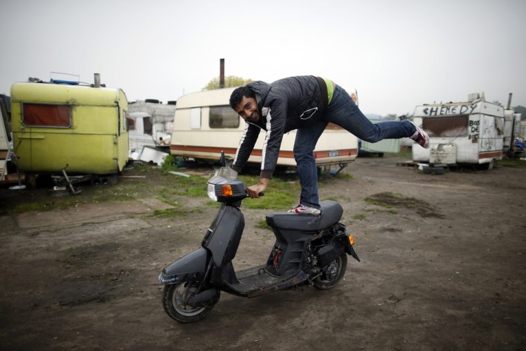 A Roma man balances on a scooter in front of caravans at an encampment of Roma families in Triel-sur-Seine.