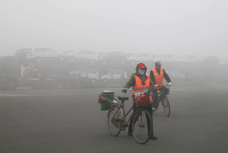 Passersby cycle past a truck waiting outside a closed toll booth as heavy smog spreads on a highway, forcing vehicles to wait in Jilin, northeast China's Jilin province on Oct. 22.