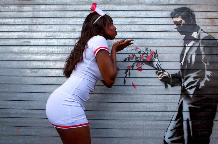 A dancer poses with a new installation of art by British graffiti artist Banksy painted on the front door of the Hustler Club in New York, Oct. 24, 2013.